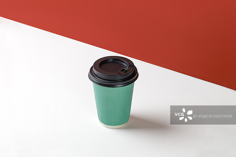 绿色纸杯与咖啡在白色的背景和红色的墙。一次性纸杯特写。空白的文本空间，模型图片素材