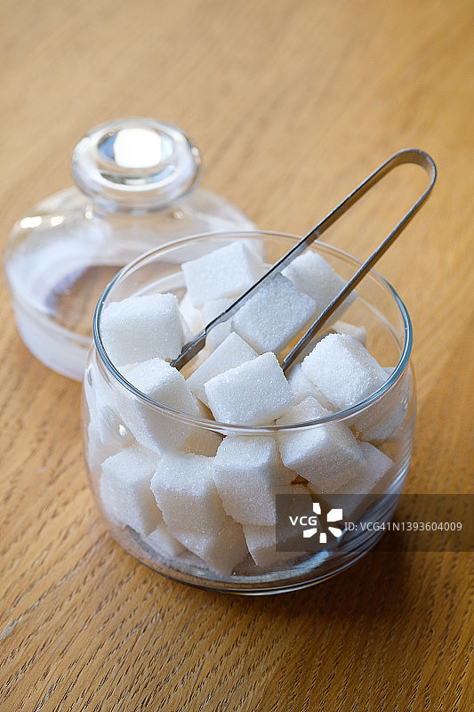 在家里，在咖啡馆，自助餐厅或餐馆里，把方糖放在透明的玻璃糖碗里，放在木桌或背景上。营养不良和生活方式的概念。图片素材