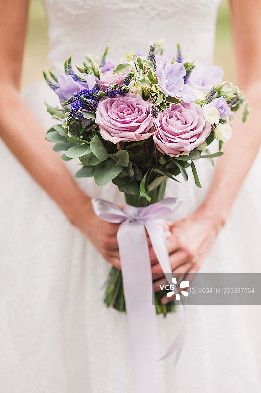 身穿白色婚纱的白人女子手里拿着一束紫色的花。图片素材