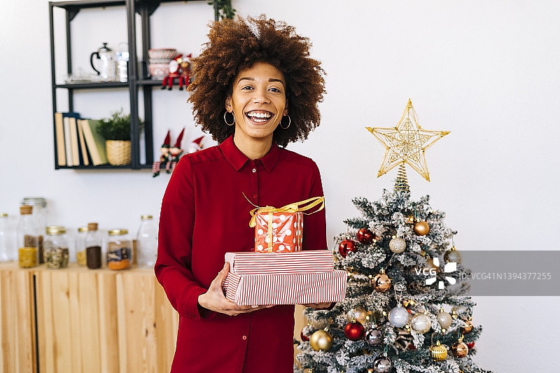 快乐的女人带着礼物站在家里的圣诞树旁图片素材