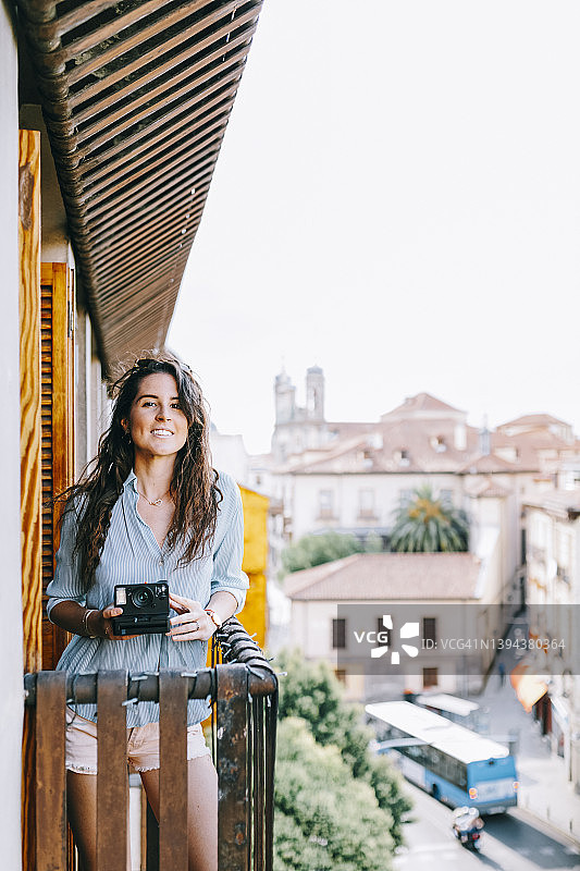 微笑的年轻女子与即时照相机站在阳台上图片素材
