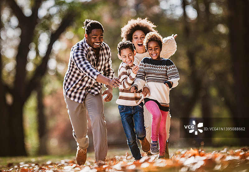 快乐的黑人父母在秋天追逐他们的孩子。图片素材