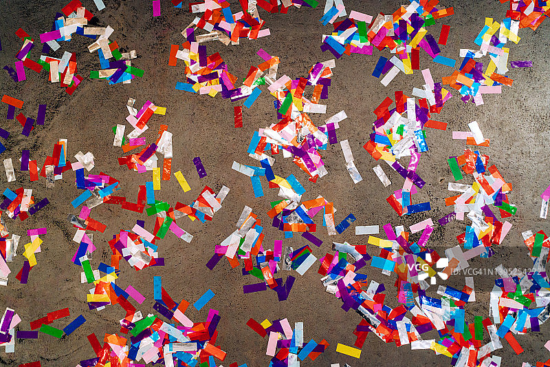 派对结束后，水泥地上撒满了五颜六色的彩纸。庆祝活动结束的概念。平躺式摄影图片素材