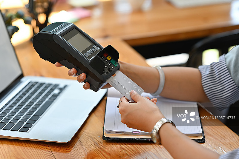 裁剪的观点，一个女人坐在办公室持有信用卡和使用信用卡刷卡机，为金融和技术的概念。图片素材