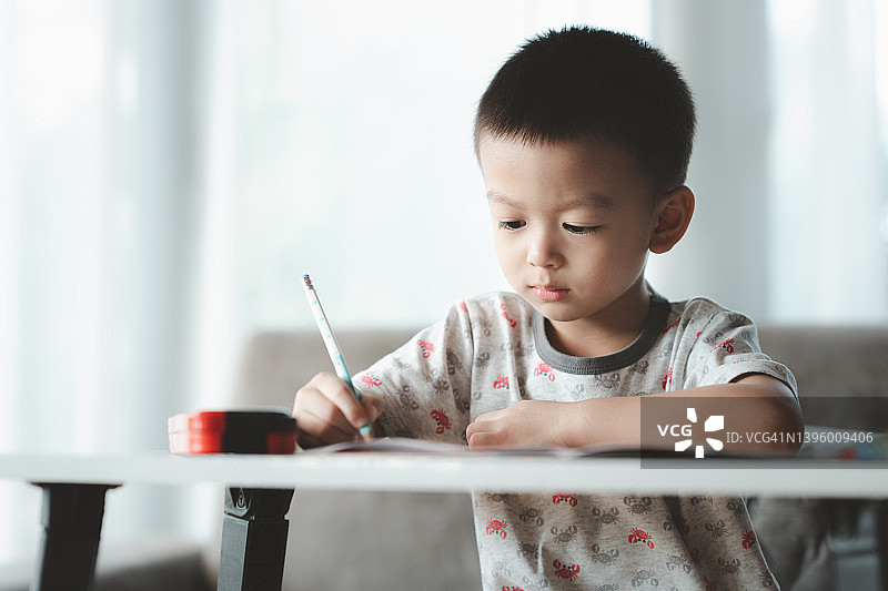 亚洲男孩用心做作业。儿童男孩拿着铅笔写字，男孩在桌子上画白纸，小学和家庭教育，远程教育的概念。图片素材