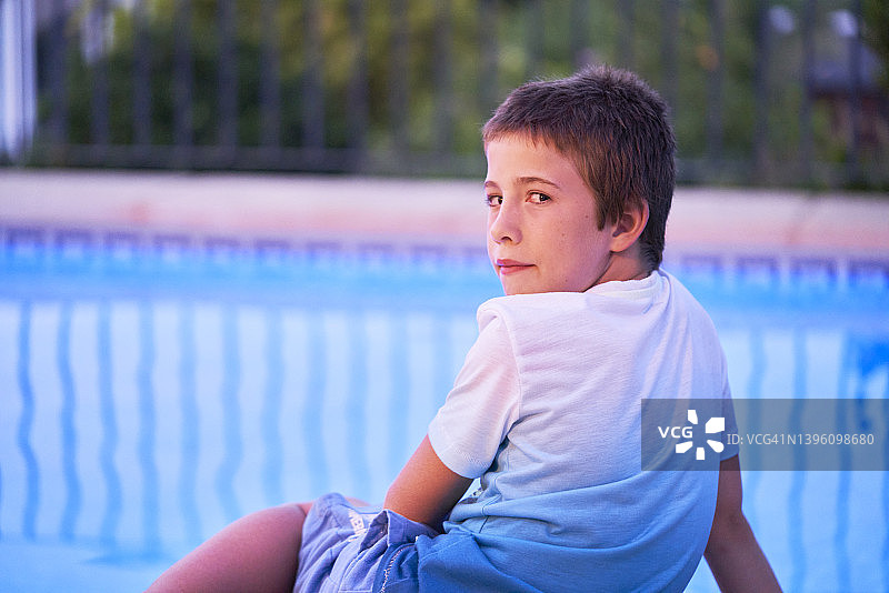 十几岁的男孩在镜头后面观看，坐在游泳池边上图片素材