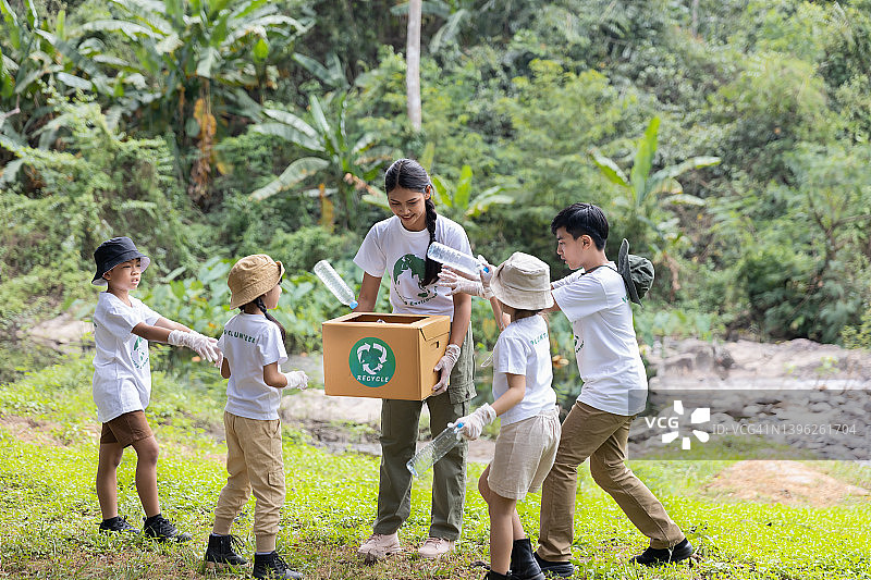 分组的孩子们自愿一起把塑料瓶收集到回收箱里。图片素材