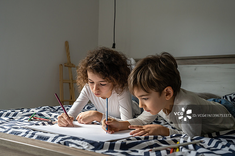 小男孩和小女孩在家里的纸上画画，两个孩子的兄弟姐妹或朋友躺在床上用蜡笔休闲和教育真实的人的家庭概念复制空间图片素材