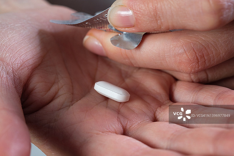 白色胶囊或药片在一个女孩或女人的手和手掌上，近距离。服用维生素、止痛药、药物和膳食补充剂。疾病预防与治疗的概念，保健与医药。计划怀孕。图片素材