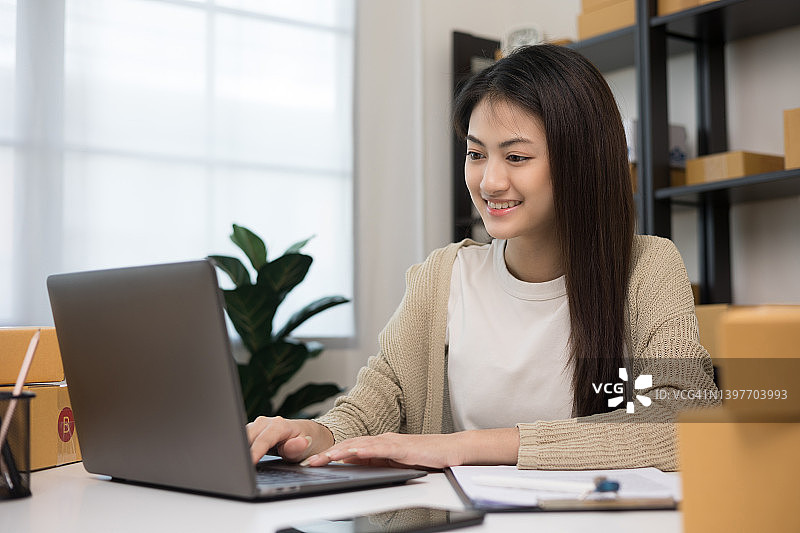 年轻的亚洲女企业家检查库存产品注意笔记本电脑。女商人工作中小企业在线在家里。请检查包裹上的地址。小企业主开始自由职业的概念。图片素材