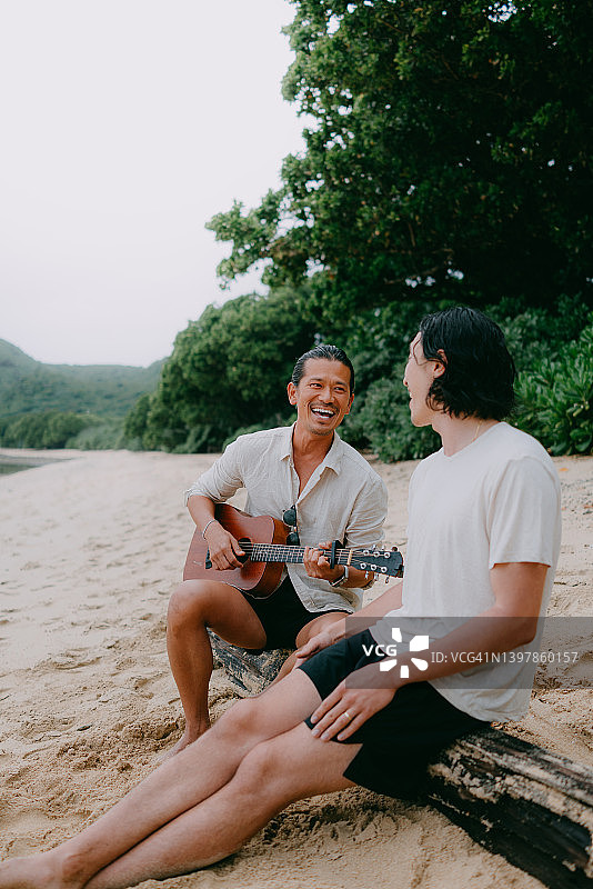 黄昏时，男人在沙滩上弹吉他唱歌图片素材