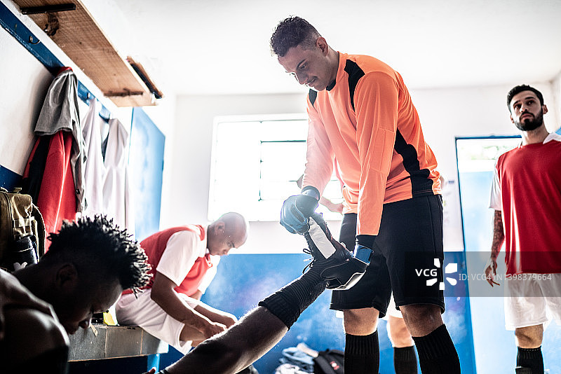 守门员在更衣室帮助一名足球运动员伸展身体图片素材