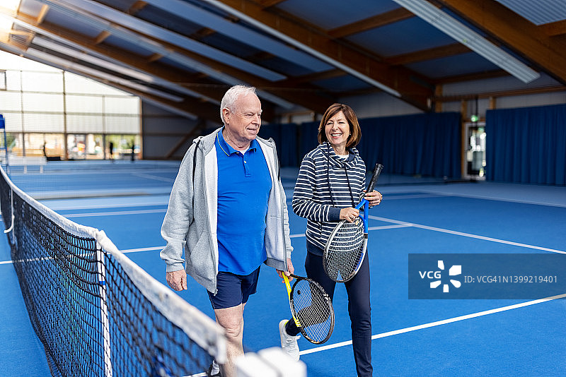 活跃的老年夫妇穿着运动服在室内网球场散步图片素材