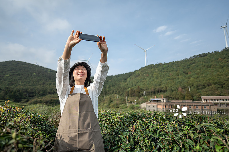 一名亚洲女茶工在茶林中用手机拍照图片素材