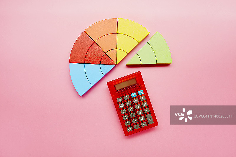 高角度的饼图由彩色的积木和红色的计算器在粉红色的背景图片素材