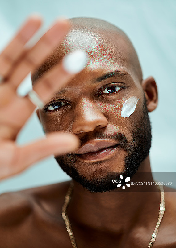 一个举手的非裔美国男模特的肖像。他的手指和眼睛下面有润肤露。那个男人独自站在房间里图片素材