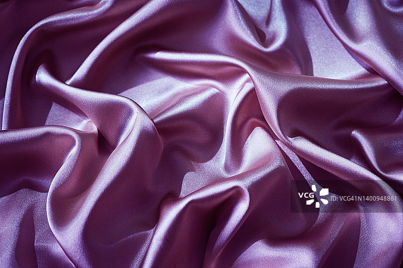 紫粉色的真丝缎子。闪亮的织物。波浪褶皱。美丽的淡紫色背景与设计空间。图片素材