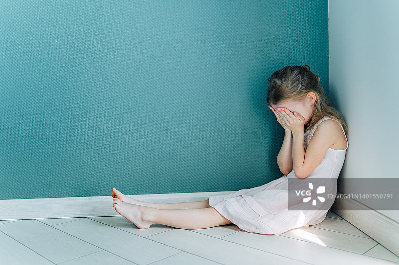 小伤心沮丧的金发女孩穿着白裙子坐在室内角落的地板上。本空间图片素材