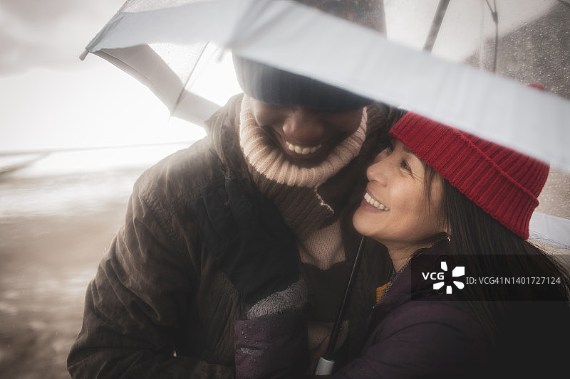 在潮湿的冬季海滩上打着伞的幸福情侣图片素材