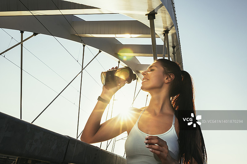 健身女子喝瓶装水。肌肉发达的年轻女性在户外锻炼后休息。图片素材