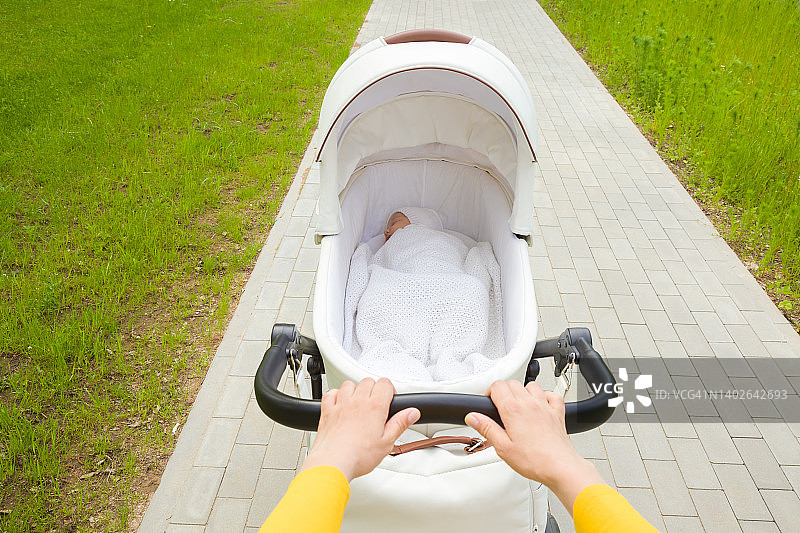 年轻的成年母亲推着白色婴儿车和新生儿在人行道上。每天在户外散步，呼吸新鲜空气。在温暖的夏日与婴儿共度时光。特写镜头。视角拍摄。图片素材