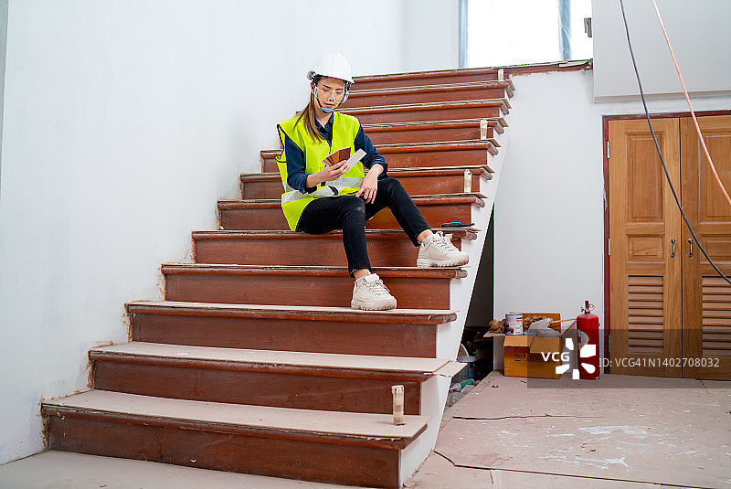 亚洲职业女性工程师或经理坐在建筑工地的楼梯上，处理彩色图表图片素材