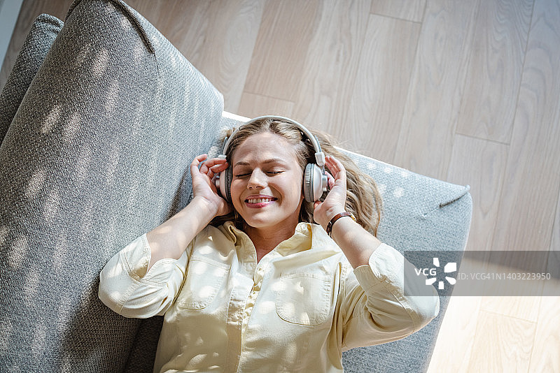 年轻快乐的女人戴着耳机听音乐，在家放松图片素材