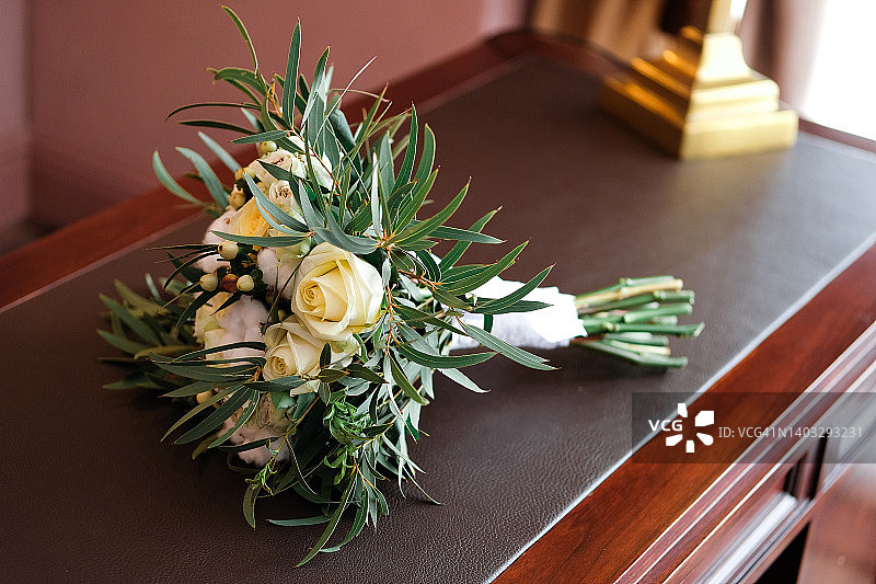 一张漂亮的婚礼花束放在桌子上，抽屉柜或床头柜上，特写。花束不同的花和绿叶，用缎带系着，背景模糊。婚礼的主题。白玫瑰和棉花的完美结合。图片素材