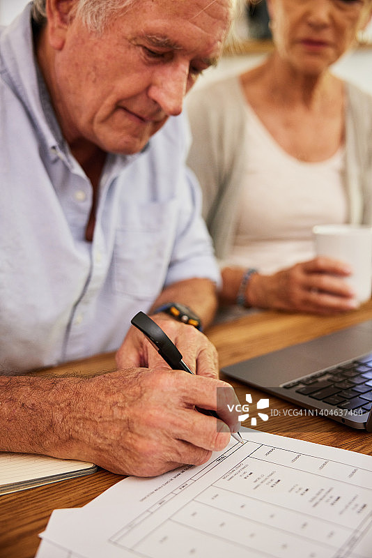 一位老人一边和妻子处理家庭财务一边签医疗账单图片素材