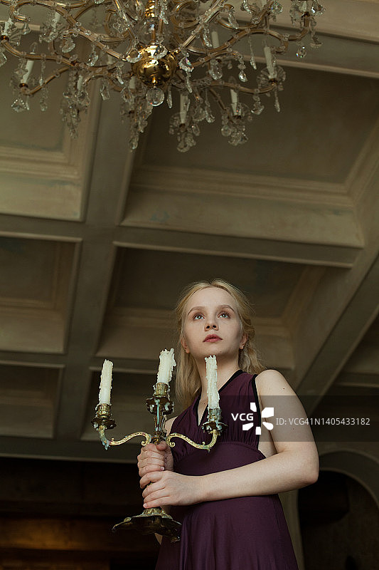 年轻女子手持吊灯与蜡烛在复古豪华室内图片素材