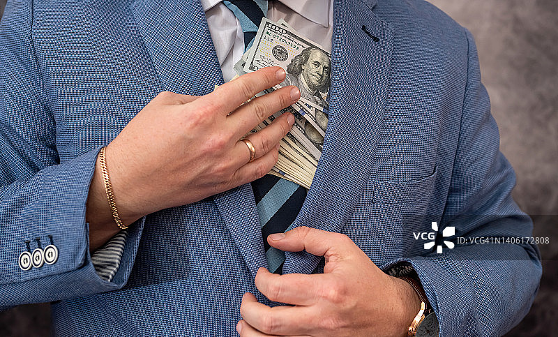 一位穿着优雅昂贵西装的高级官员把抢来的钱放进了自己的口袋。图片素材
