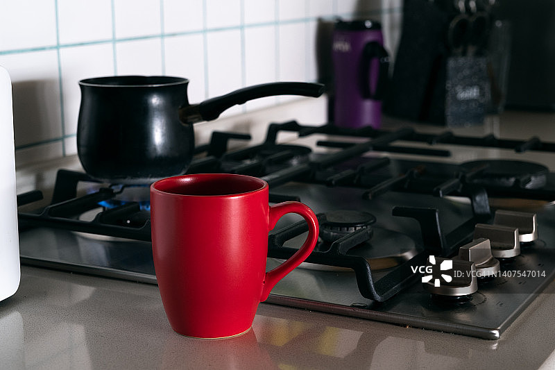咖啡是在煤气炉上用土耳其壶煮的，在火上。为早餐煮咖啡。制作土耳其咖啡的土耳其人，在家里的厨房或招待所。旁边有一个明亮的杯子。做你自己。家庭生活。图片素材