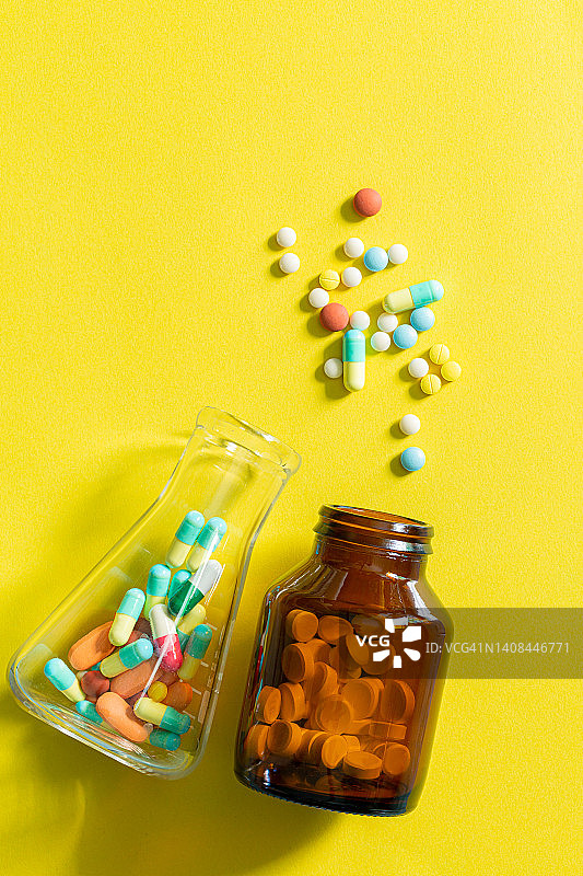 药片和药丸瓶在黄色背景，多色药片和药丸胶囊从玻璃瓶在黄色背景堆各种各样的药物药片和药丸。医疗特写图片素材
