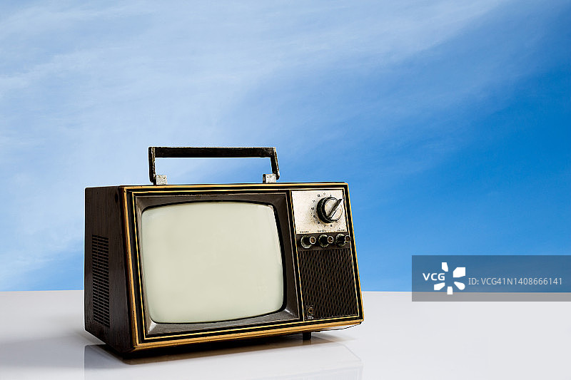老式的电视在白色的桌子与蓝色的天空背景。复古的电视技术图片素材