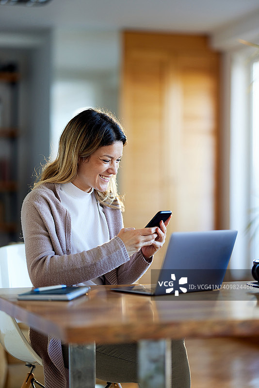 快乐的女人在家里工作时使用手机。图片素材