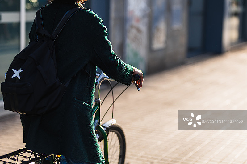 女子背双肩包和骑自行车在日落在城市商业区的后视图。图片素材