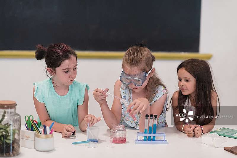小学科学课堂:热情的老师向不同的孩子们讲解化学，小男孩在烧杯中混合化学物质。孩子有兴趣地学习图片素材