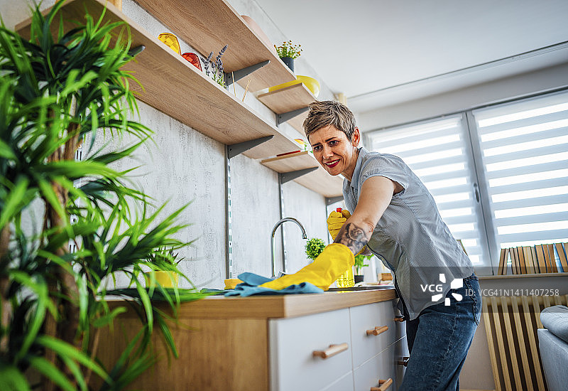 妇女喷洒厨房柜台和清洁它图片素材