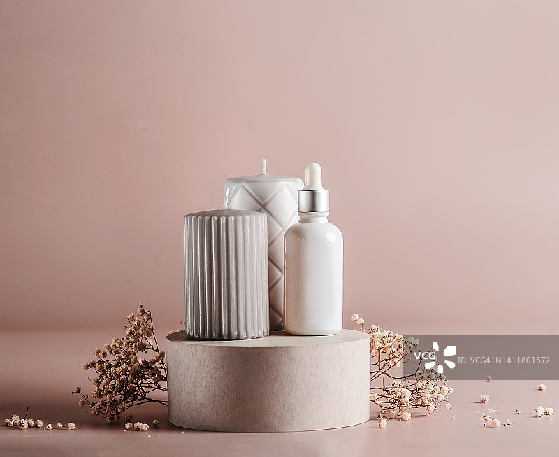 化妆品和皮肤护理的概念与蜡烛，移液管瓶和花圆筒讲台在苍白的米色背景。图片素材