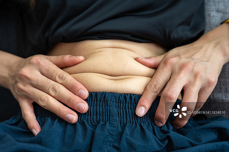 特写不明身份的人触摸肥胖的腹部。图片素材