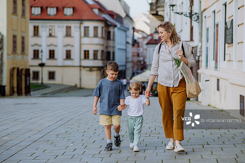 年轻的母亲带着零废物购物袋和她的孩子们手牵着手走在城市的街道上图片素材