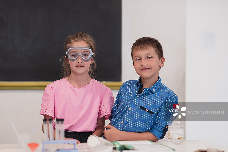 小学科学课堂:热情的老师向不同的孩子们讲解化学，小男孩在烧杯中混合化学物质。孩子有兴趣地学习图片素材