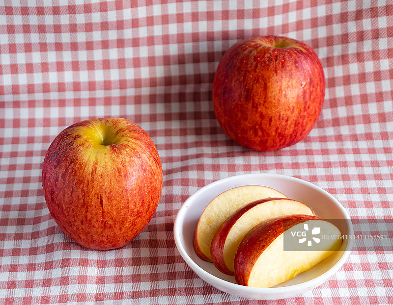 两个红苹果放在粉红色的格子布上。把苹果片放在白色盘子里。图片素材