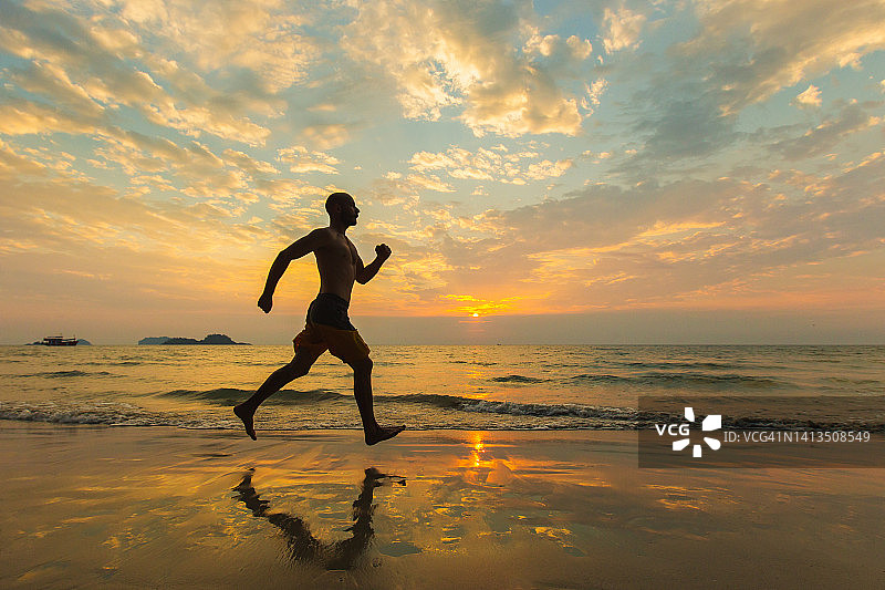 运动男子在日落时赤脚在沙滩上跑步。健康和积极的生活。图片素材