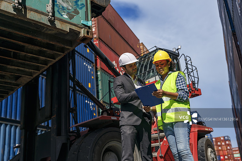 年轻领班与工人共同工作，负责企业物流、进出口运输或货物运输集装箱仓库的运输过程控制。图片素材