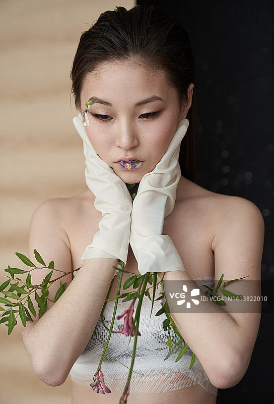 美丽的亚洲女人特写，拿着她的脸，她的手在大橡胶手套。图片素材