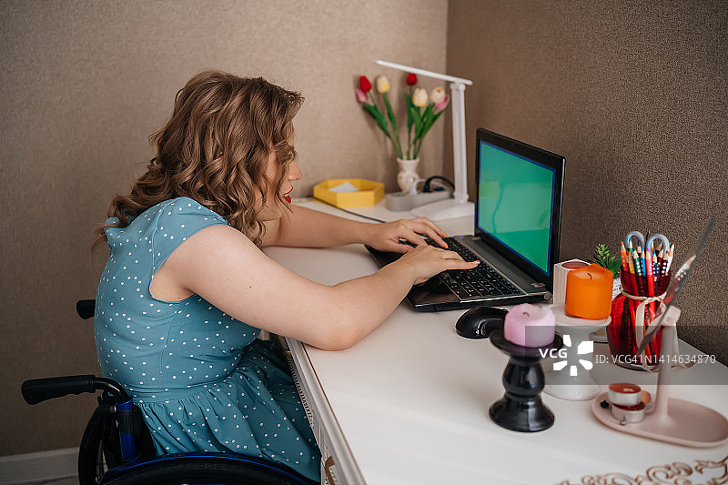 脑瘫女孩坐在轮椅上用笔记本电脑在家在线学习图片素材