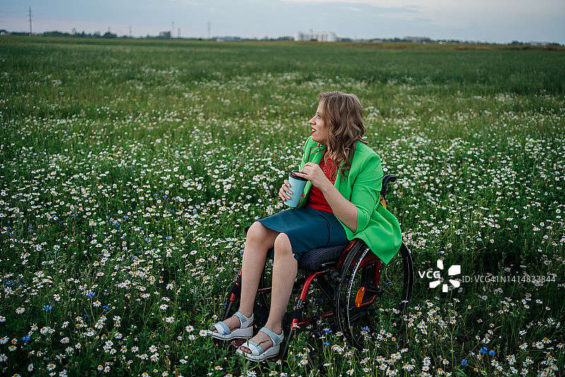 坐在轮椅上的脑瘫女孩在甘菊田喝咖啡图片素材