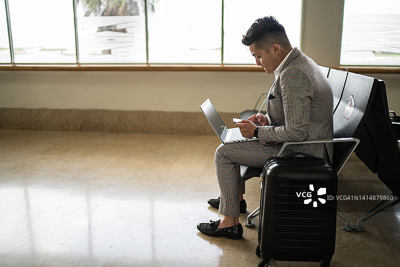 商务人士在机场离境区使用手机和笔记本电脑图片素材