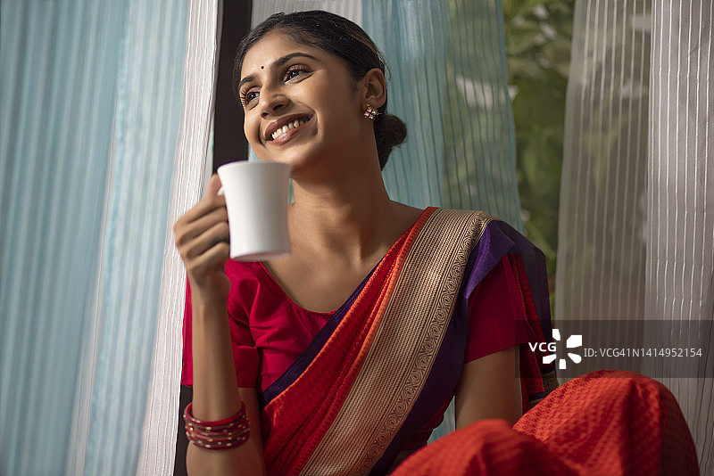 快乐的女人坐在窗边喝着咖啡，看着外面图片素材